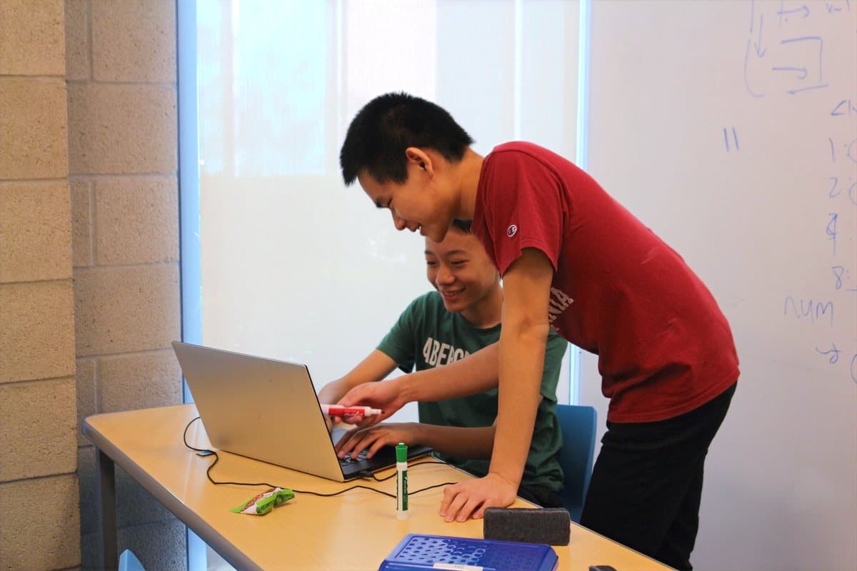 A coding coach working through code with a student at a laptop.